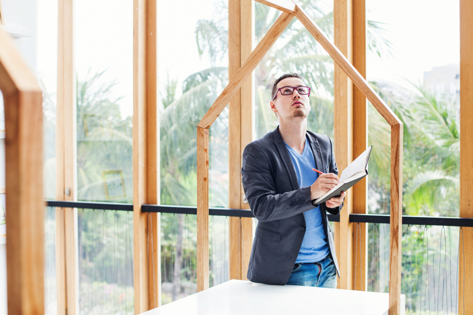 young engineer looking at a empty frames in a villa with tropical garden and writing something at his copybook